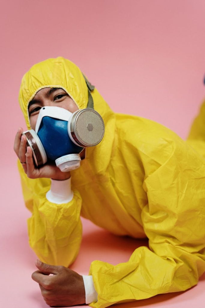 Asian man in protective gear with respirator on pink background.
